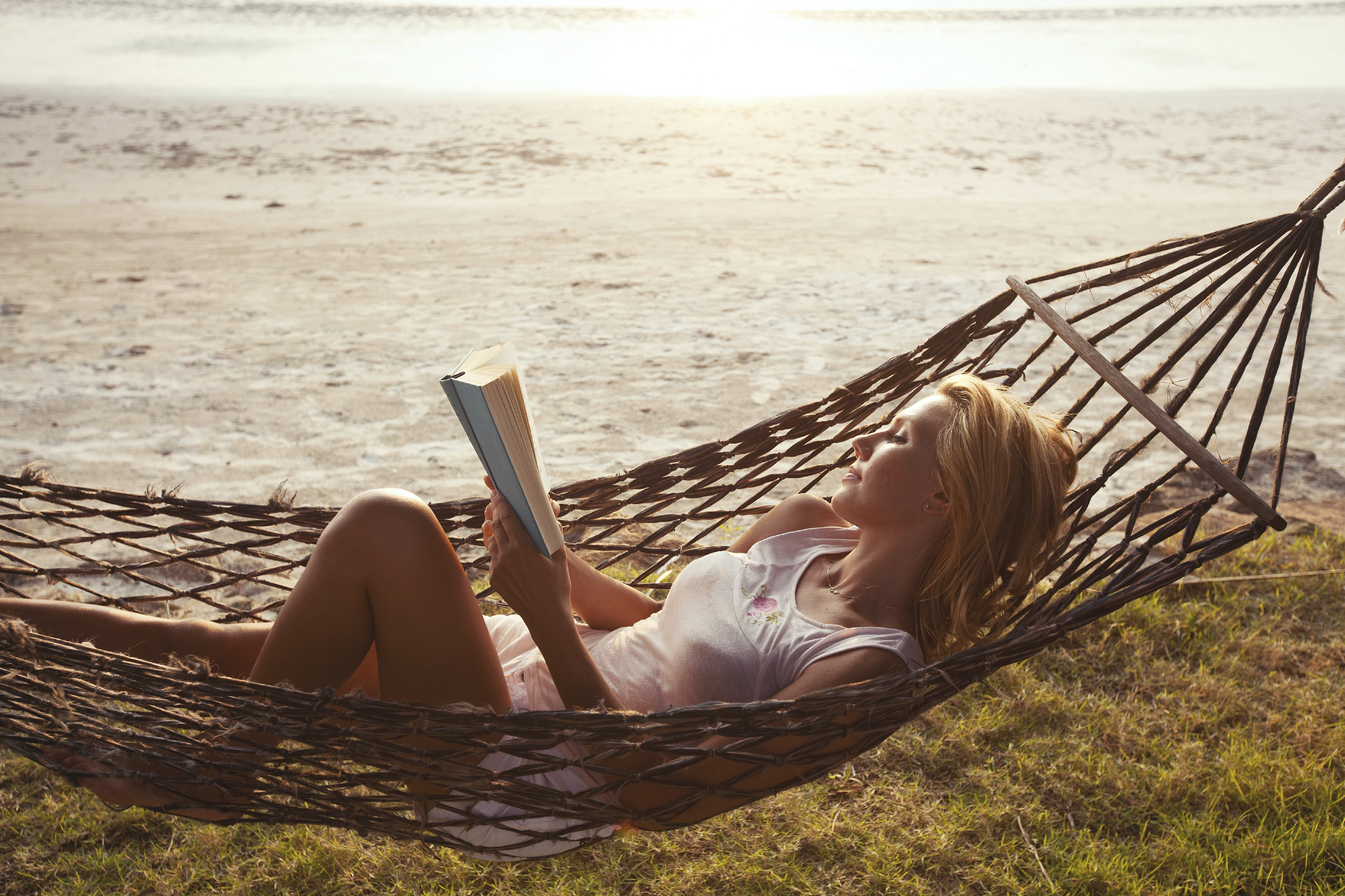 woman reading book in hammock on the beach